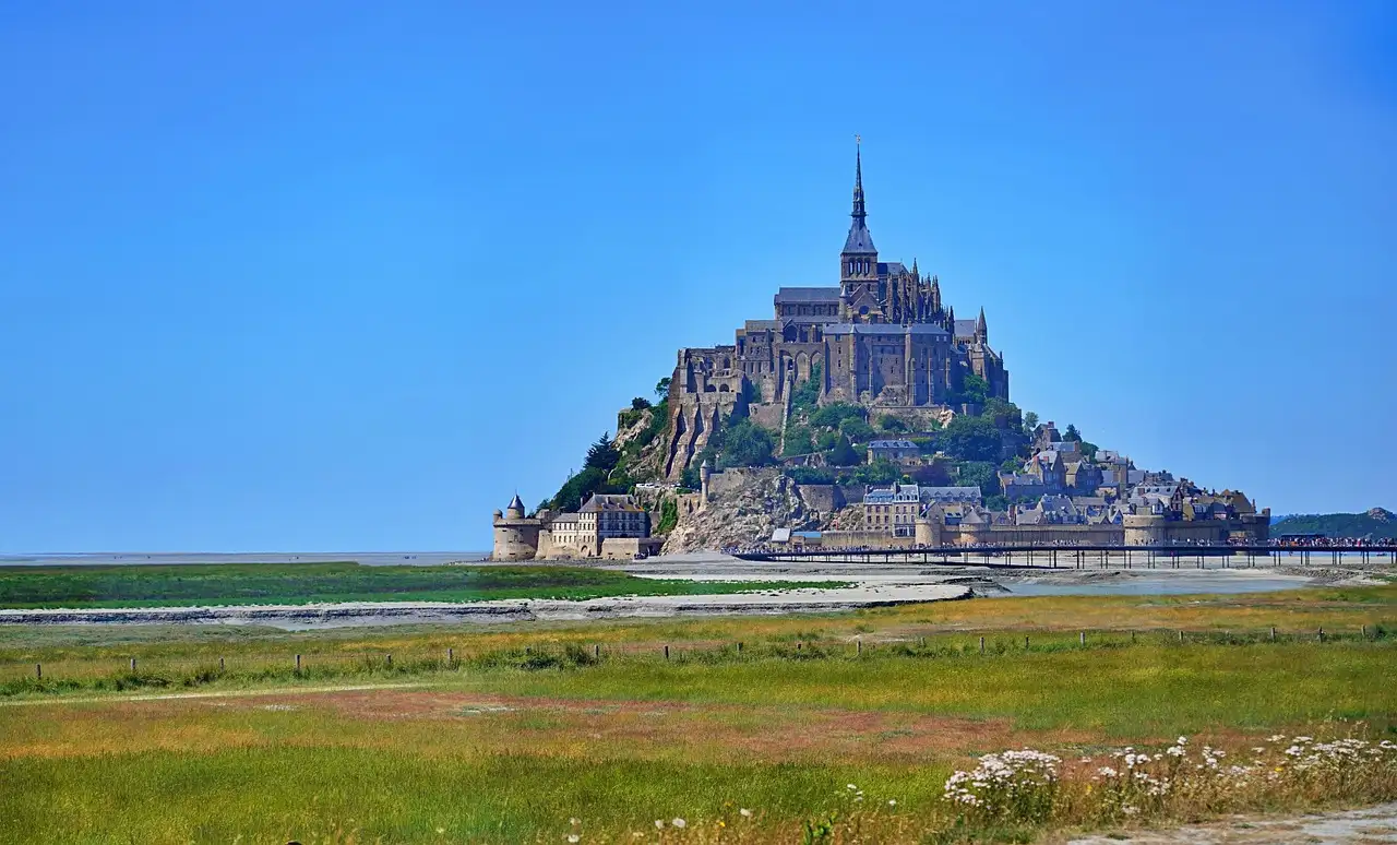 Mont Saint-Michel abbey rising from the bay under a blue sky behind a meadow