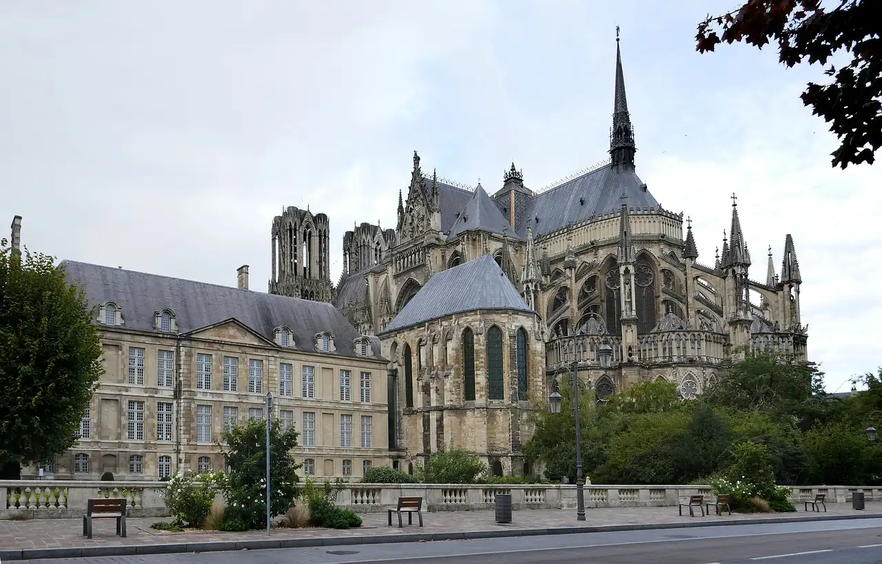 The Gothic cathedral of Reims rising behind a stone building and trees