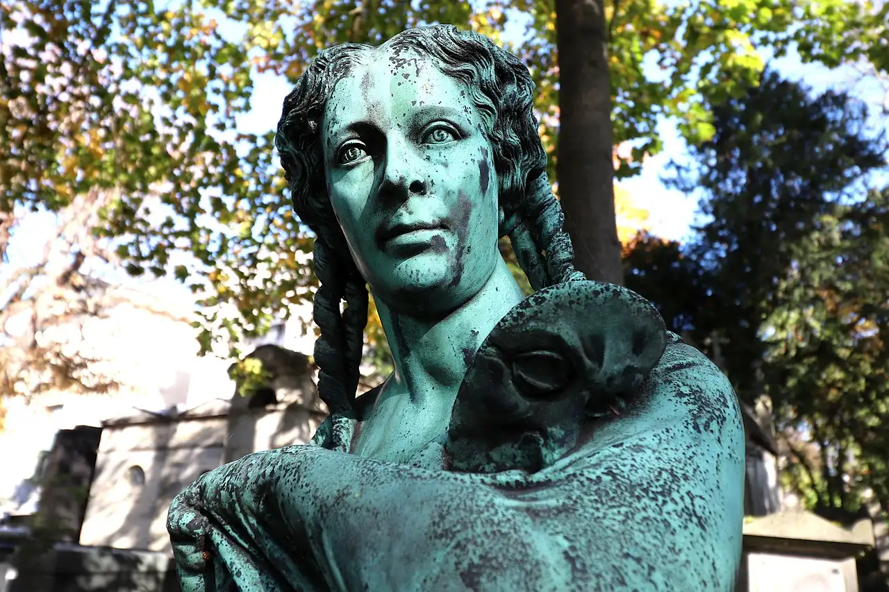 A weathered bronze statue on a tomb in Père Lachaise Cemetery