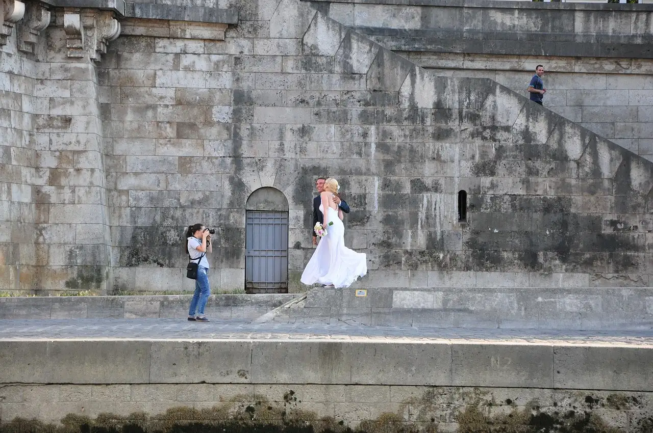 A photographer shooting a couple posing on a stone quay of the Seine