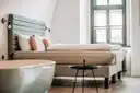 A bright hotel room with a made double bed and a tall window