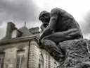 Rodin's bronze The Thinker in front of a stone mansion under a grey sky