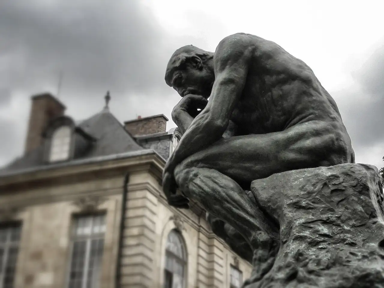 Rodin's bronze The Thinker in front of a stone mansion under a grey sky