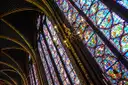 Close view of a tall stained-glass window in the Sainte-Chapelle upper chapel, with red and blue picture panels
