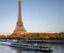 A glass-roofed cruise boat on the Seine with the Eiffel Tower behind it