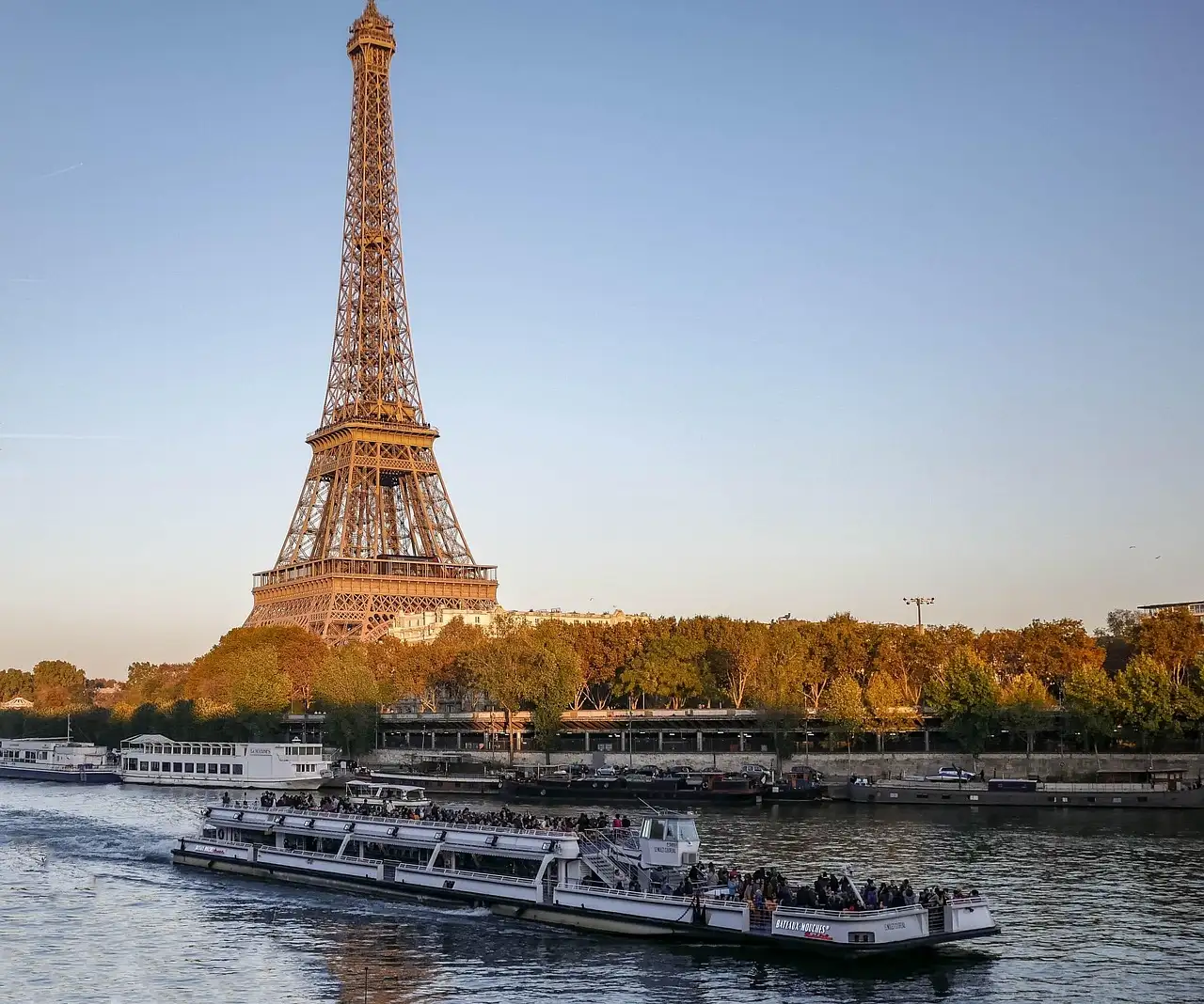 A glass-roofed cruise boat on the Seine with the Eiffel Tower behind it