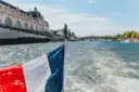 View from a boat on the Seine, a French flag over the wake and the Musée d'Orsay on the bank