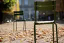 Green metal chairs on a leaf-strewn gravel path in the Tuileries Garden