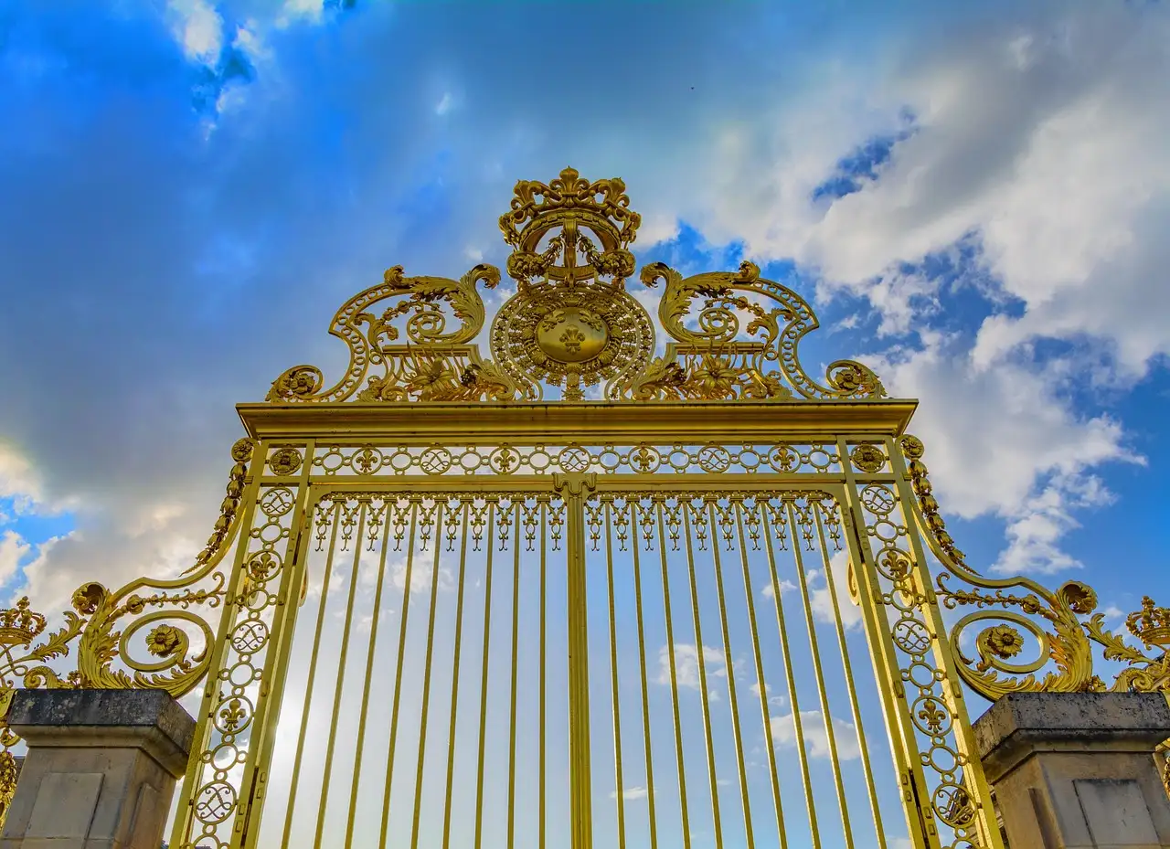 The gilded Royal Gate at the entrance to the Palace of Versailles against a blue sky