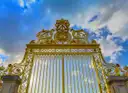 The gilded Royal Gate at the entrance to the Palace of Versailles against a blue sky