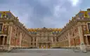 The brick-and-stone Marble Courtyard of the Palace of Versailles under grey clouds