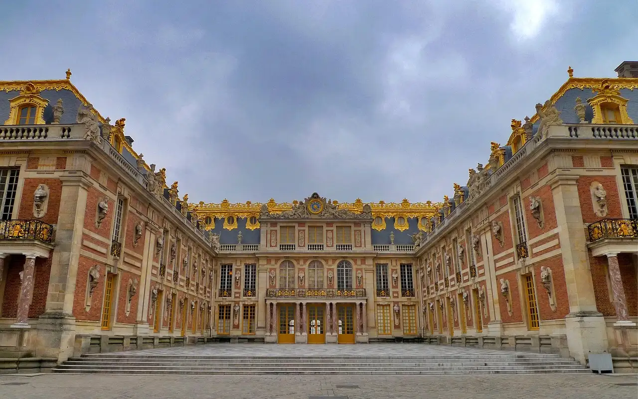 The brick-and-stone Marble Courtyard of the Palace of Versailles under grey clouds