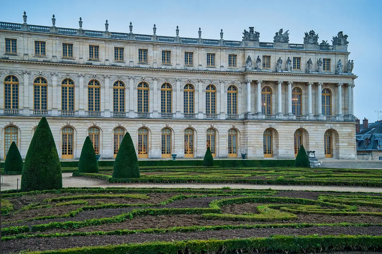 The garden front of the Palace of Versailles behind clipped parterres under a blue sky