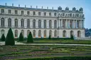 The garden front of the Palace of Versailles behind clipped parterres under a blue sky